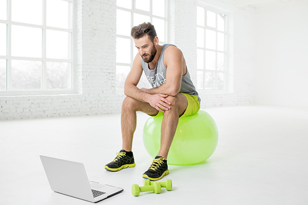Image of a man sitting on an exercise ball looking at a laptop